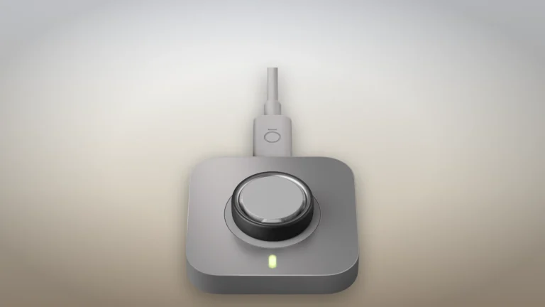 Oura Ring 5 seated on its supplied charging dock with the cable attached and the dock status light showing green